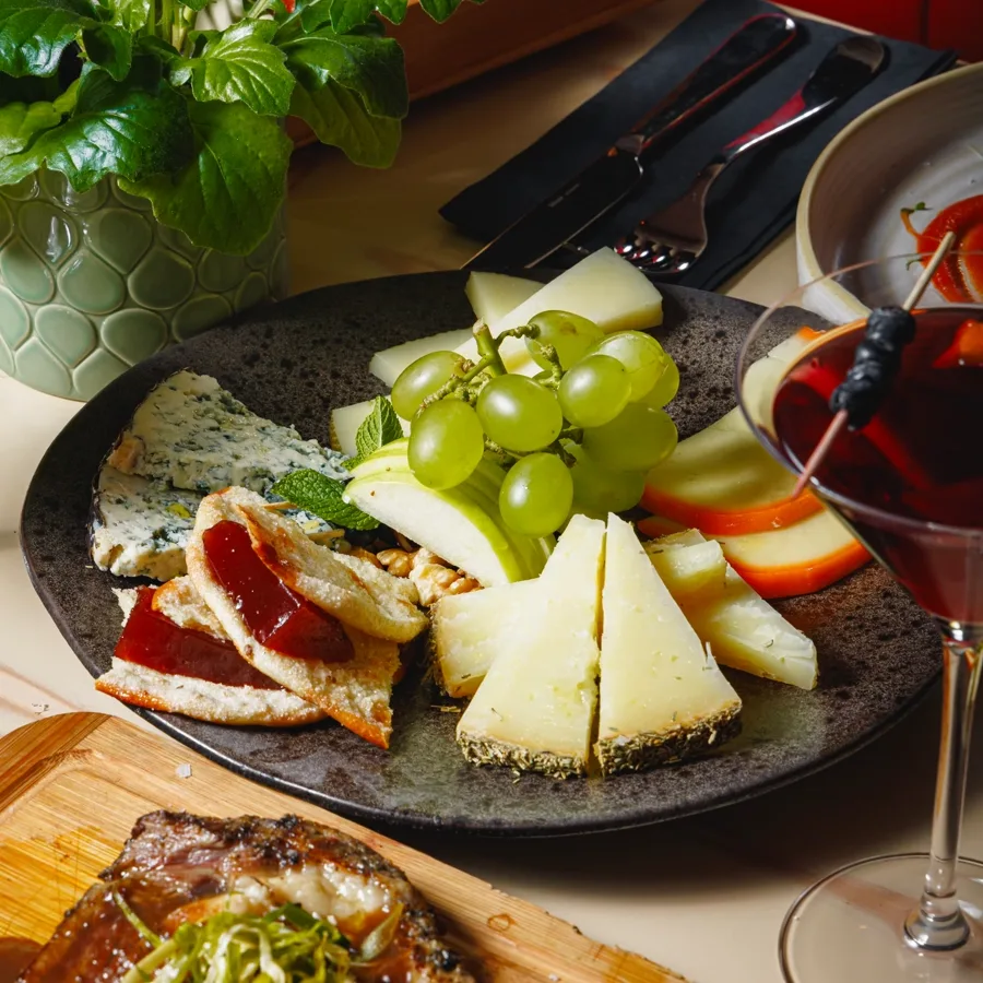A cheese platter with grapes, apple and membrillo
